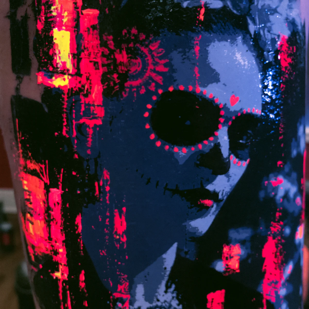 Single Dia de los Muertos portrait with painterly graffiti quality, dominated by red and yellow on the left and blue on the right.